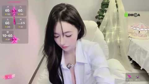 Media: A video of an Asian woman with long black hair, wearing a white lab coat, seated indoors, with a festive Christmas tree and white decorations in the background.