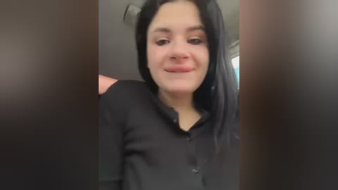 Video of a young woman with long black hair, wearing a black long-sleeved shirt, smiling slightly, in an indoor setting.