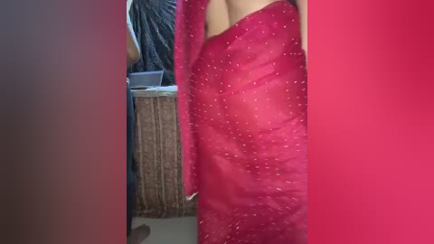 Media: Video of a woman in a vibrant red saree with subtle white dots, holding it slightly open. Background includes a wicker basket and a partially visible cat.