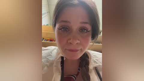 Video of a young woman with fair skin and brown hair, wearing a white shirt, taken indoors with blurred background.