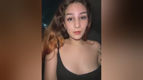 A video of a young woman with light skin, brown hair, and a black tank top. She has a septum piercing and a tattoo on her left shoulder. The background is blurred, emphasizing her face.