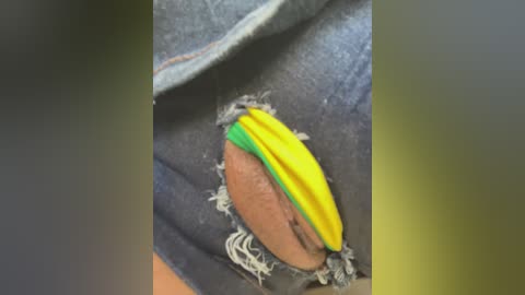 Media: Video of a yellow and green striped fabric patch sewn onto a ripped denim pocket. The patch is vibrant and contrasts with the worn denim. The texture of the fabric is smooth, while the denim shows fraying edges.