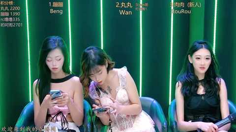 Video of three young East Asian women with long black hair, dressed in sleeveless tops, seated in a row, engrossed in smartphones, against a dark green, glowing vertical panel background.