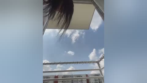 Media: A video of a person's head and shoulder, with dark hair, taken from a low angle, looking up at a cloudy sky and a balcony railing.
