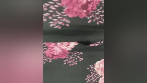 A close-up video of a dark-skinned person with a shaved head, standing in front of a wall adorned with large pink and white flowers. The background is blurred, emphasizing the subject's presence.