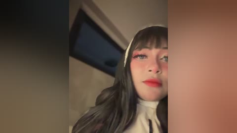 Media: Video of a woman in a nun costume with long black hair, wearing white habit and veil, blushing, and looking to the side. Background shows a dimly lit room with a window.