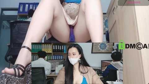 Media: A video of an Asian woman with long black hair wearing a white face mask, beige jacket, and high-heeled sandals, sitting at a cluttered office desk.