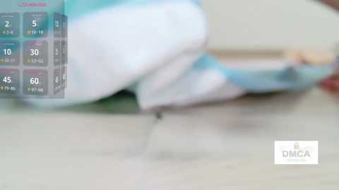 A blurry video of a child with light skin, wearing a white and turquoise shirt, lying on a tiled floor, partially covered by a blue and white blanket. The background is indistinct.