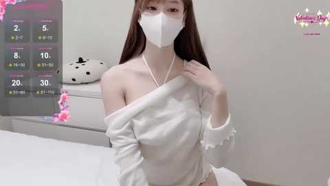 Media: Video of an Asian woman with long, straight brown hair, wearing a white off-shoulder sweater, white mask, and white panties, posing indoors against a white background.
