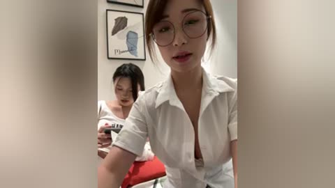 Video of two Asian women in a clinic; one with glasses, wearing a white blouse, and another with short hair, in a white shirt, both texting.