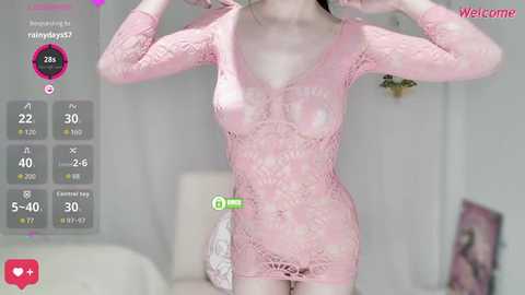 A video of a light-skinned woman in a pink, see-through lace bodysuit, posing indoors with a smartphone screen overlay showing stats.