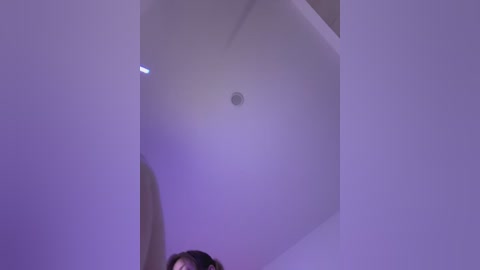 Video of a woman with short dark hair, partially visible, standing under a low, white ceiling with a circular light fixture.