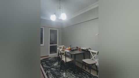 A video of a dimly lit, sparsely furnished room with beige walls, a black and white patterned rug, a wooden dining table, and four chairs, featuring a double door with a frosted glass panel.