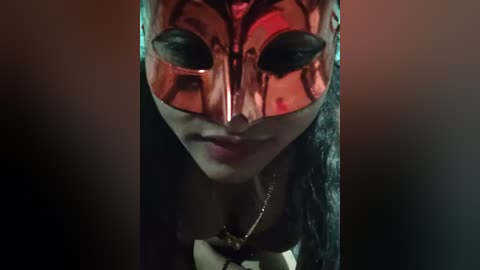 Video of a masked woman with a reflective, blood-red Venetian mask, featuring intricate patterns, and a dark, wavy hairstyle. The background is dark and blurred, emphasizing the mask's shiny texture.