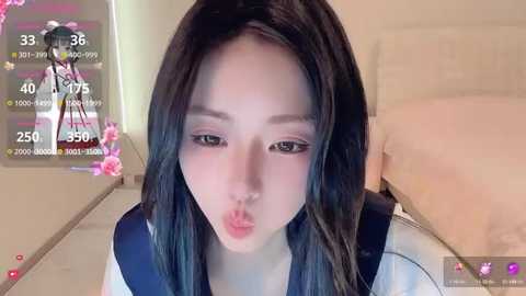 Video of a young Asian woman with long black hair, pouting, wearing a school uniform in a bedroom with a bed and pink floral decor.