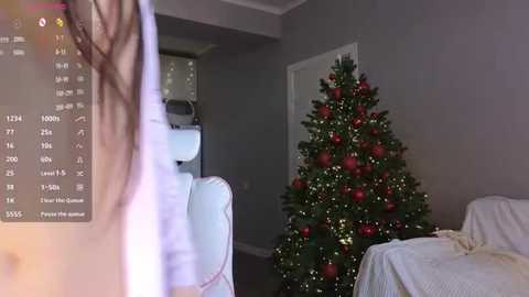 Video of a living room with a decorated Christmas tree, a person's shoulder visible on the left, and a smartphone screen displaying weather information.