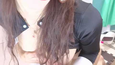 A video of a woman with long, wavy brown hair, wearing a black shirt, kissing a man's bare chest, revealing a light-skinned, hairy chest. Background shows a white sink and green cloth.
