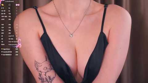 A video of a woman in a black, low-cut, spaghetti-strap dress, showcasing a large, intricate cat tattoo on her left arm. The background features a blurred curtain and a social media app screen with various icons and notifications.