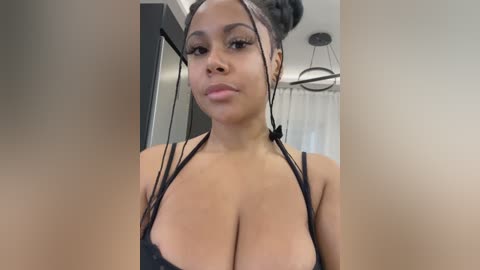 Video of a young Black woman with a medium skin tone, large breasts, and a slender build, wearing black lingerie, standing indoors with a modern interior background.