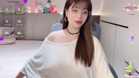 Video of a young woman with pale skin, brown hair, and glasses, wearing a white off-shoulder top, sitting in a brightly lit room with plush toys, digital interface, and a \"Vintagewhore\" watermark.