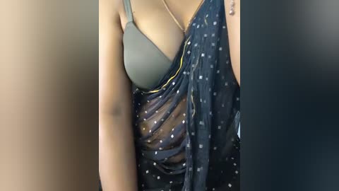 Video of a person wearing a gray bra under a sheer, navy blue sari with white polka dots, against a blurred beige background.