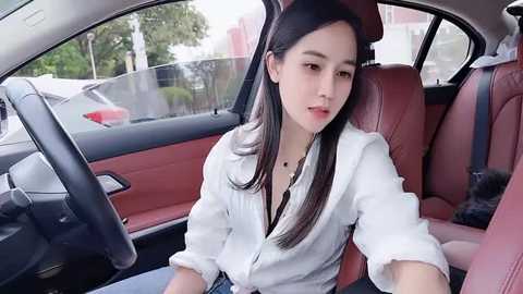 A video of an East Asian woman with long black hair, fair skin, and a slender physique, wearing a white button-up shirt, sitting in the driver's seat of a red car with a leather interior.
