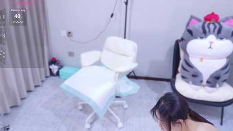 Video of a minimalist room with a white office chair, a plush grey cat cushion, and a person with long dark hair in the foreground.
