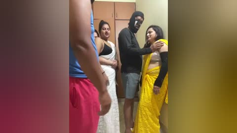 Video of an intimate moment between a man and a woman in a home setting. The man, in a black shirt and shorts, fondles the woman's breast in a yellow sari.