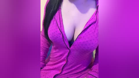 Video of a woman with long, straight black hair, wearing a low-cut, magenta zip-up hoodie that reveals cleavage. Her skin is light, and the background is a gradient of purple hues.