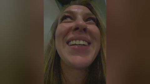 Video of a Caucasian woman with long, light brown hair, smiling widely with her teeth showing, captured from a low angle, emphasizing her open expression.