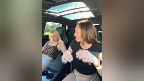Video of a blonde woman in leopard-print bikini top, lying unconscious in a car seat, while a brunette woman in a black top and beige pants, wearing a seatbelt, sits beside her, looking concerned.