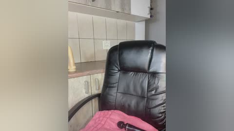Video of a modern kitchen with a black leather office chair, a beige dildo on a counter, and a pink blanket draped over the chair.