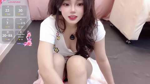 Video of an East Asian woman with long black hair, wearing a white T-shirt with colorful patches, sitting on a bed, smiling, with a virtual reality headset on.