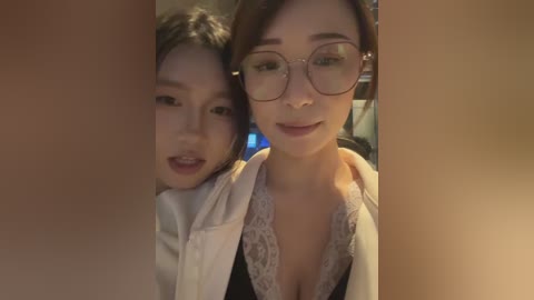 Video of two young Asian women with light skin, one with glasses and the other with a floral top, smiling closely, with blurry background.