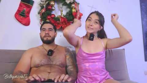Media: Video of a muscular, tattooed man and a slim, long-haired woman in festive attire, both wearing black headphones, sitting on a beige sofa, surrounded by holiday decorations.