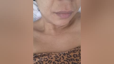 A close-up video of a woman's partially bare upper torso, showing her collarbone and a hint of cleavage, wearing a leopard-print bra. Her fair skin is smooth with visible pores, and her lips are slightly parted.