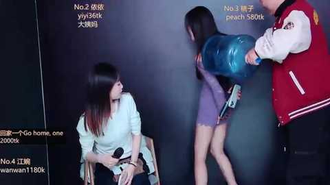 A video captures a young woman in a light shirt, seated, and a woman in a blue dress, being restrained by a man in a red varsity jacket.