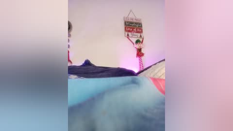 A blurry video of a girl lying on a bed, covered in blue and pink blankets, with a colorful wall decal and a stuffed animal in the background.