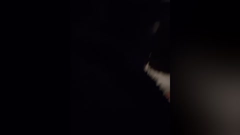 A dimly lit video featuring a close-up of a woman's mouth, partially obscured by shadows. Her lips are slightly parted, revealing a hint of teeth and tongue. The background is almost entirely black, emphasizing the subject.