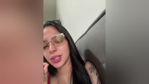 Media: A video of a young Asian woman with long black hair and glasses, wearing a red top, sitting on a gray couch. She is talking on a phone, with a tattoo visible on her shoulder.