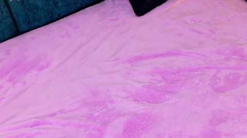 Video of a bed with a pink, swirling, liquid-like surface, resembling a lava lamp, covering the mattress. The background features a dark teal headboard.