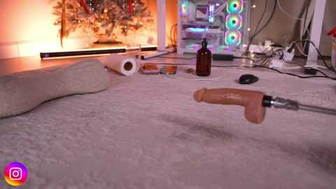 Video of a messy room with a cream rug, a naked man lying on it, a dildo, a brown bottle, and a Christmas tree in the background.