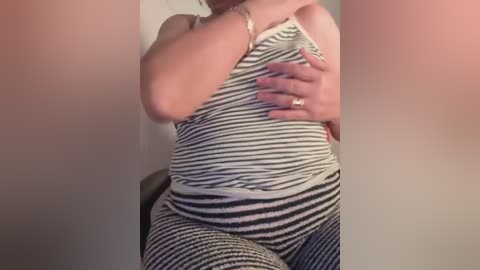 Video of a person in a black-and-white striped tank top and matching pants, holding their chest, against a plain background.