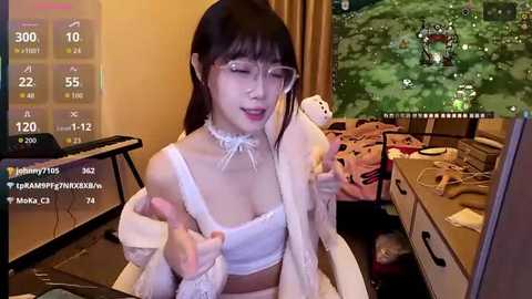 Video of an East Asian woman with glasses, wearing a white choker and lingerie, sitting in a messy room with a gaming PC, monitor, and plush toys.