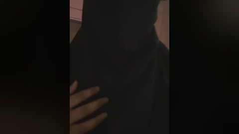 A dimly lit video captures a person wearing a black dress, with a hand gently touching their waist. The background is blurred and dark, creating a mysterious and intimate atmosphere.