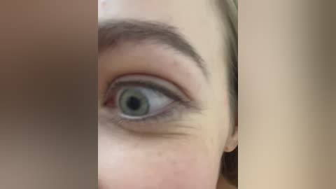 Close-up video of a Caucasian woman's left eye, showing a clear, blue iris, thick dark lashes, and slightly arched eyebrows. The background is blurred, focusing attention on the eye.