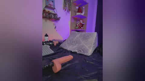 A dimly lit video shows a messy bedroom with a dark blanket, a computer keyboard, a large dildo, and a vibrator on the bed, against a purple and blue-hued wall.