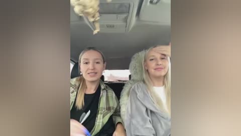 Video of two women sitting in an airplane, one with blonde hair in a ponytail, wearing a plaid shirt, and the other with long blonde hair, wearing a grey hoodie.
