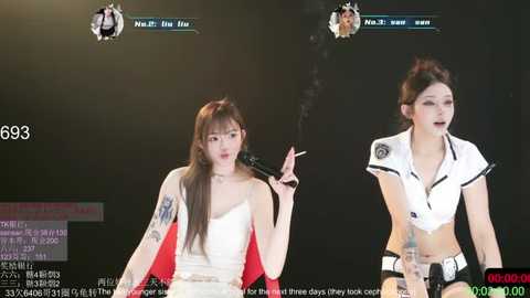 Video of two Asian women, one smoking, both wearing revealing, white, cropped tops with black accents, on a stage in front of a dark background.