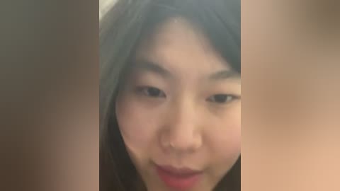 A close-up video of an Asian woman with smooth, fair skin, long black hair, and a gentle smile, surrounded by blurred, out-of-focus figures.